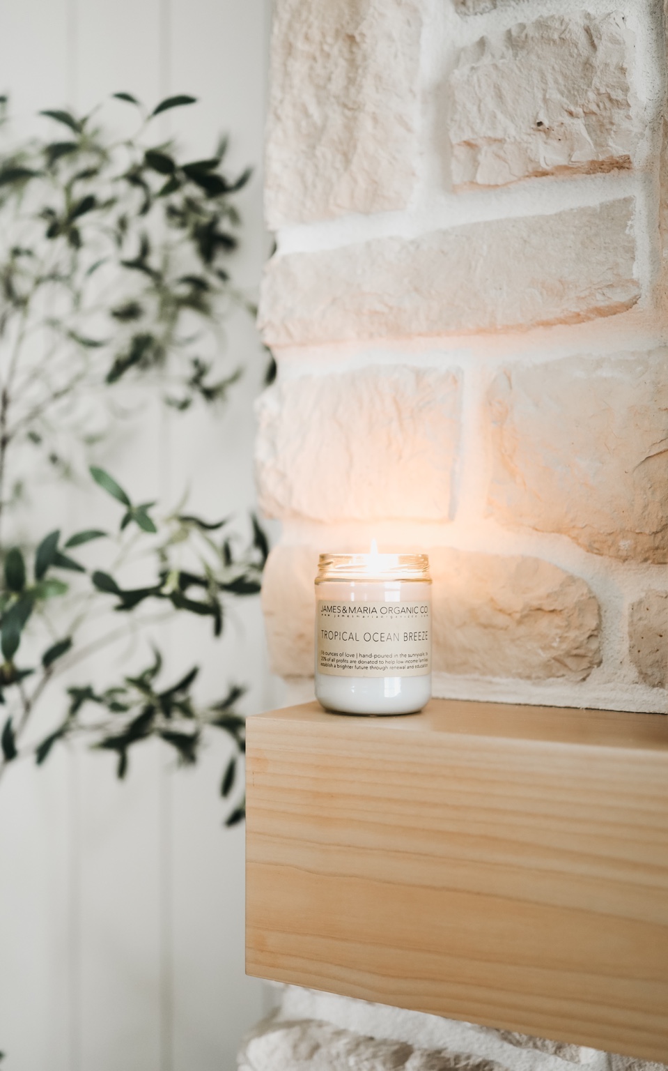 Lit candle styled on a natural wood mantel beside warm stone and greenery